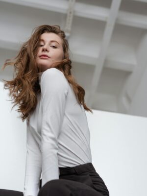 Elegant woman in a white long sleeve shirt posing indoors with a confident expression.